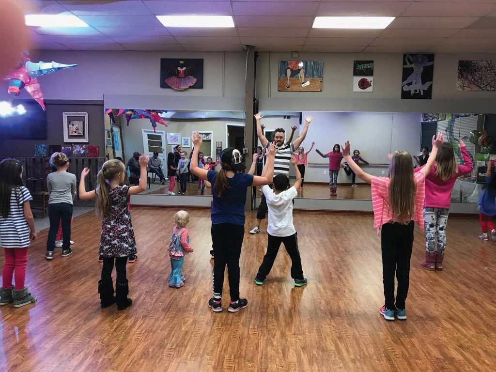 with everyone raising their arms in unison. Colorful decorations adorn the dance studio