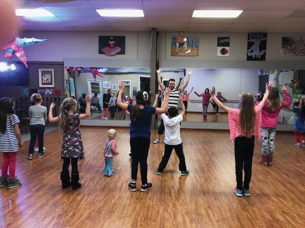 with everyone raising their arms in unison. Colorful decorations adorn the dance studio