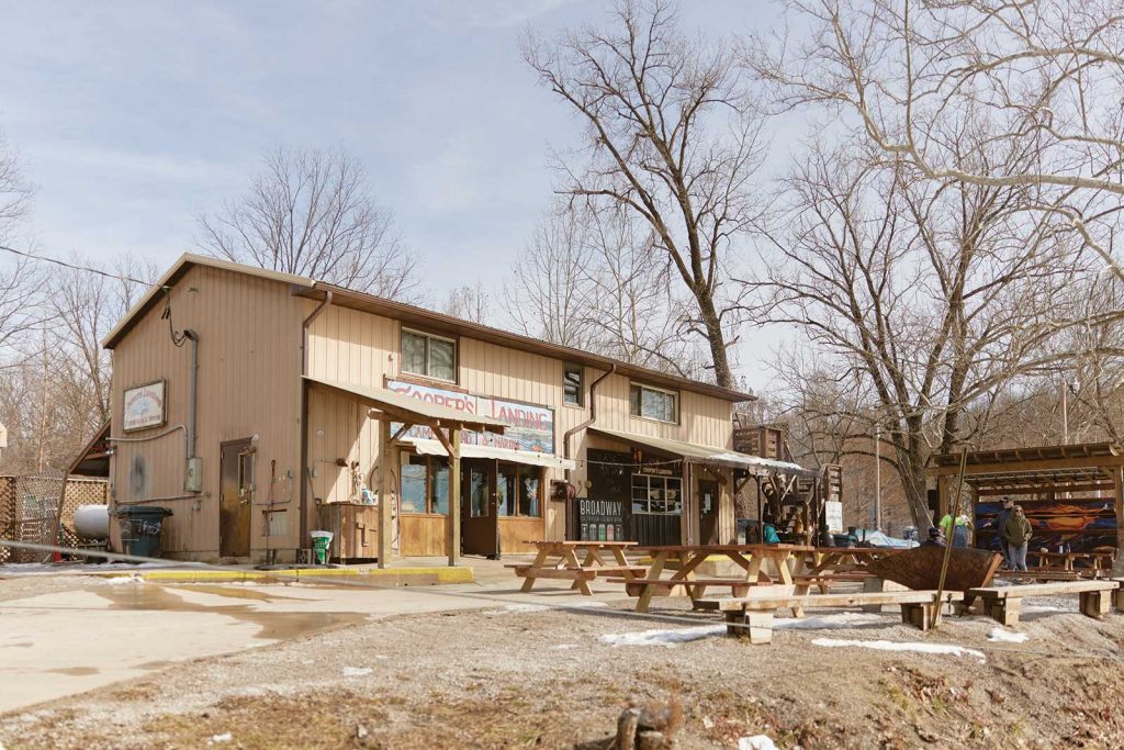 surrounded by barren trees. Picnic tables and a fire pit are in the foreground. A few people are visible near the entrance