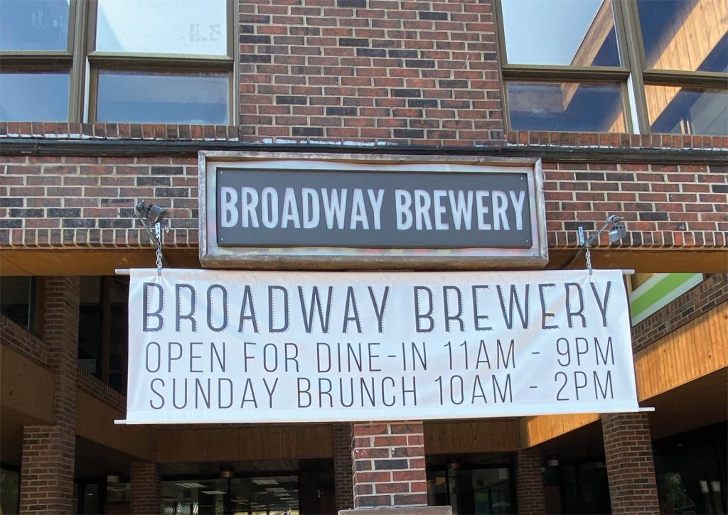 SUNDAY BRUNCH 10AM - 2PM.|A chalkboard with a red frame reads Contactless Pick Up Here in white chalk. A small flower drawing is under the text. The background shows a counter with a red