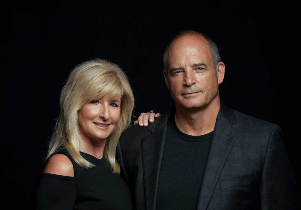 and the woman is wearing a dark suit. Both are smiling and looking at the camera.