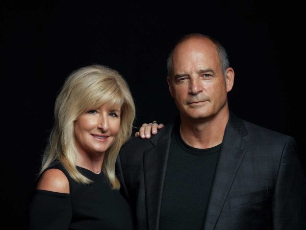 and the woman is wearing a dark suit. Both are smiling and looking at the camera.