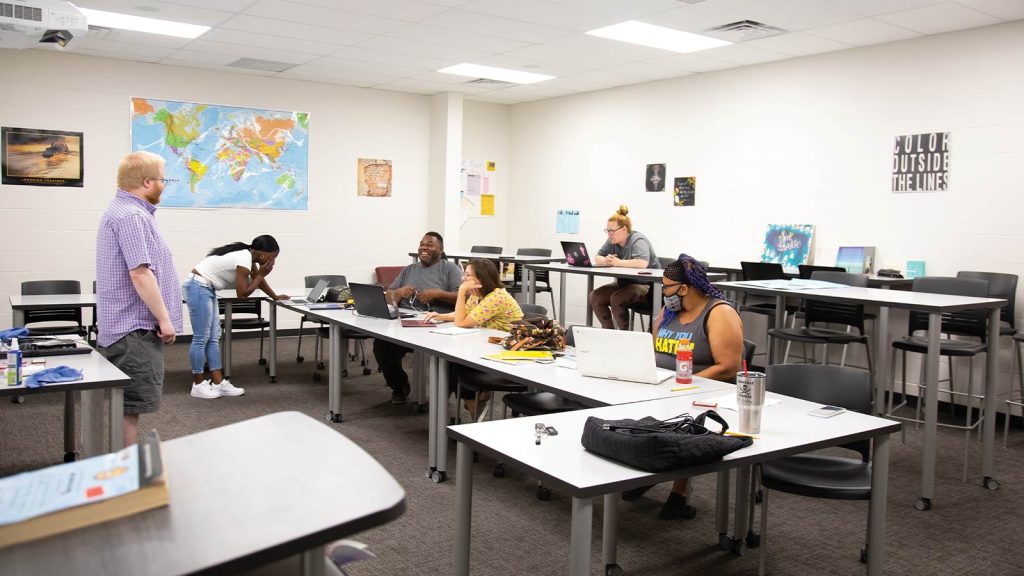 using laptops and engaging in discussion. A person stands