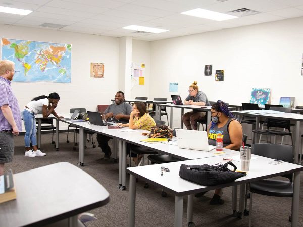 using laptops and engaging in discussion. A person stands