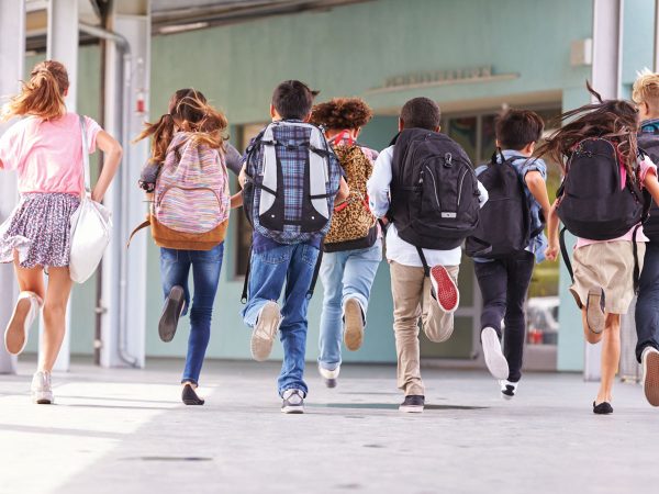 group-of-school-children-running-through-hall-with-backpacks