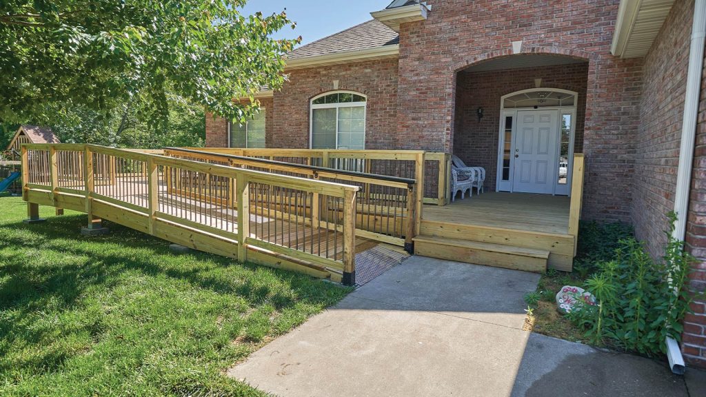 with a white door flanked by two windows. The ramp is lined with safety railings and surrounded by a grassy lawn.|Accessible bathroom with a walk-in shower