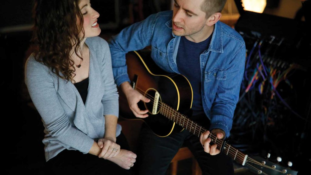playing an acoustic guitar together. The man