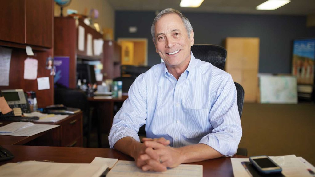 with hands clasped. The background shows office furniture