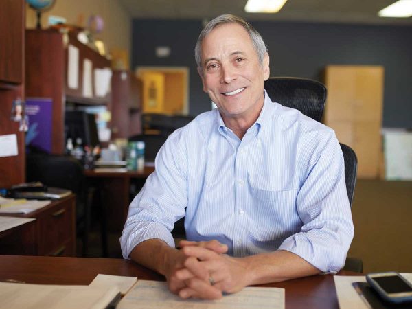 with hands clasped. The background shows office furniture