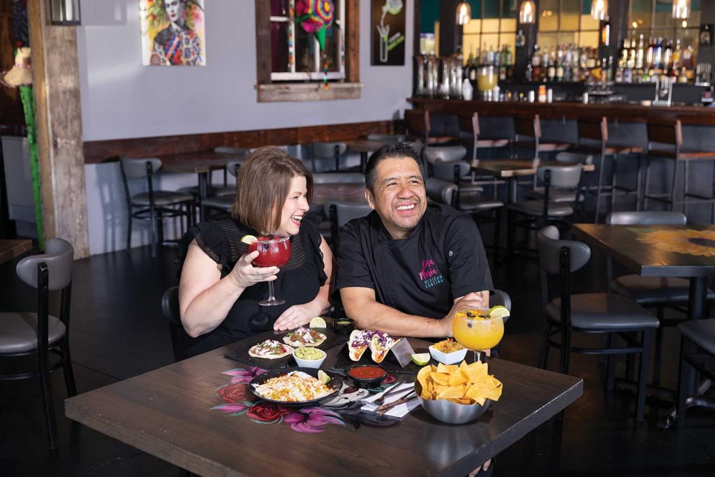 two margaritas served on the table|A couple laughing and sitting at a table in a mexican resturant with two different orders of tacos