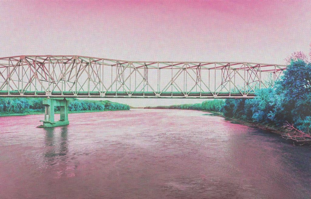 creating a dreamlike atmosphere.|A metal truss bridge spans a wide river with dense foliage on both banks. The image has a pinkish hue