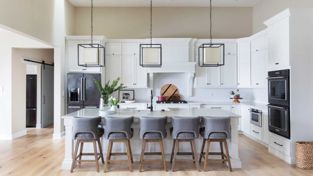 and three pendant lights hang overhead. A vase with greenery decorates the countertop.|A bright mudroom with white shiplap walls features a wooden bench with a wicker basket