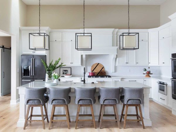and three pendant lights hang overhead. A vase with greenery decorates the countertop.|A bright mudroom with white shiplap walls features a wooden bench with a wicker basket