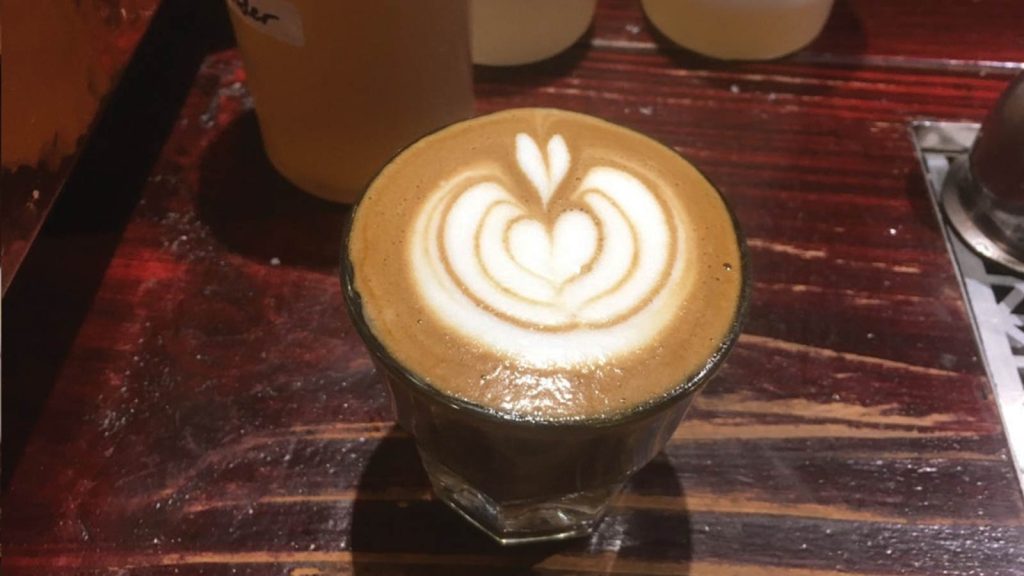 placed on a rustic wooden table.|Two cups of coffee with intricate latte art. The left cup features a leaf pattern with a heart at the tip