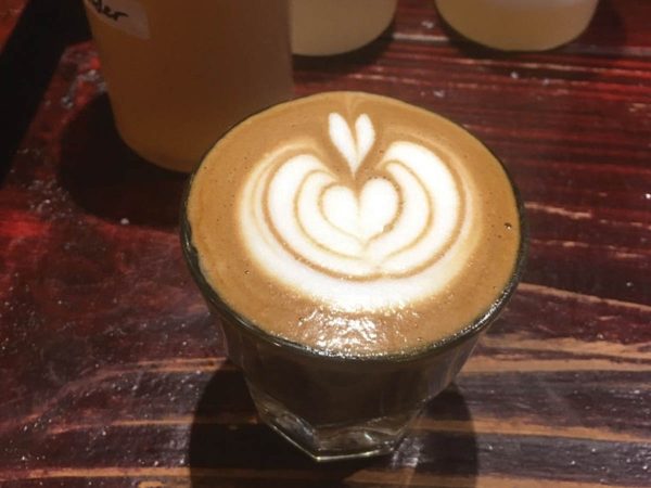 placed on a rustic wooden table.|Two cups of coffee with intricate latte art. The left cup features a leaf pattern with a heart at the tip