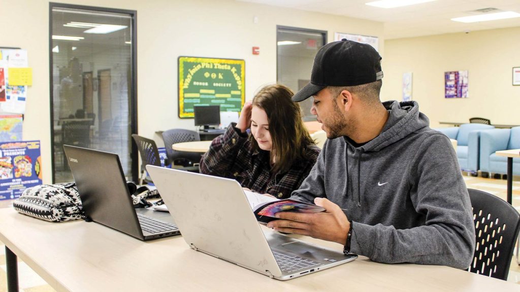 working on laptops. The female student in a plaid shirt is looking at her screen