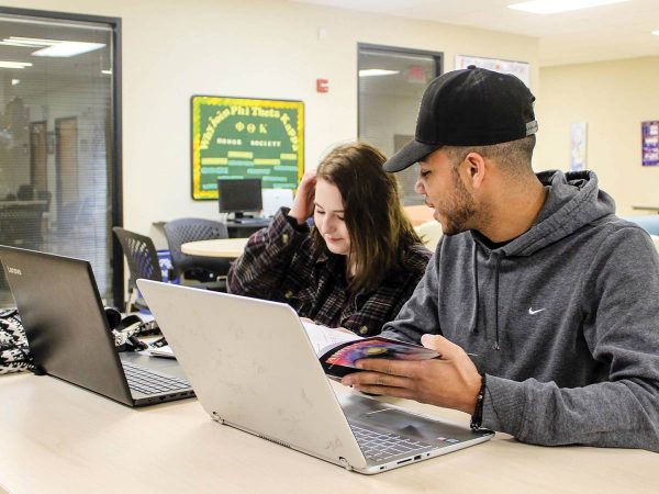 working on laptops. The female student in a plaid shirt is looking at her screen