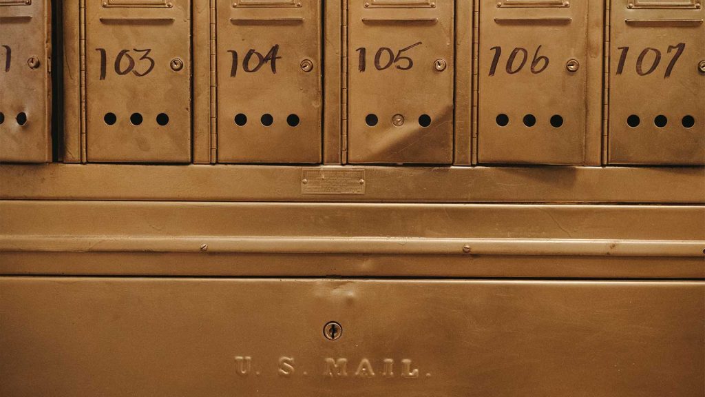 the words U.S. MAIL are engraved on a larger brass door. The mailboxes feature small ventilation holes near the bottom.|Cozy bedroom with an ornate metal four-poster bed