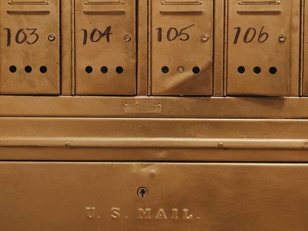 the words U.S. MAIL are engraved on a larger brass door. The mailboxes feature small ventilation holes near the bottom.|Cozy bedroom with an ornate metal four-poster bed