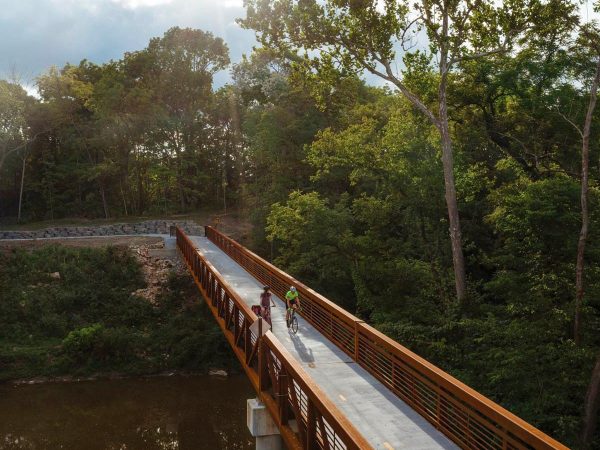 narrow bridge surrounded by lush green trees. The bridge spans over a calm river