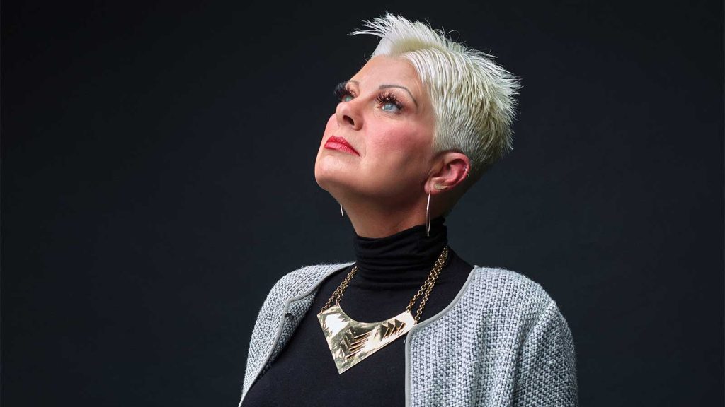 white hair looks upward. She wears a black turtleneck