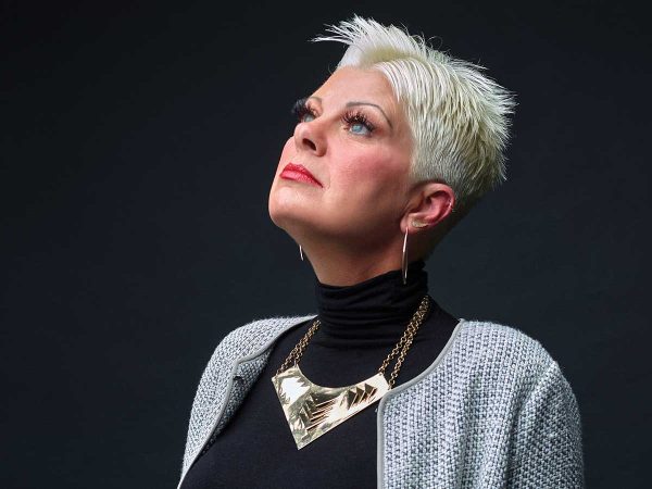 white hair looks upward. She wears a black turtleneck