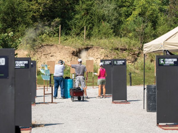 three-people-in-the-distance-aiming-at-targets-further-in-the-distance-one-man-is-adjusting-the-aim-of-the-shooter
