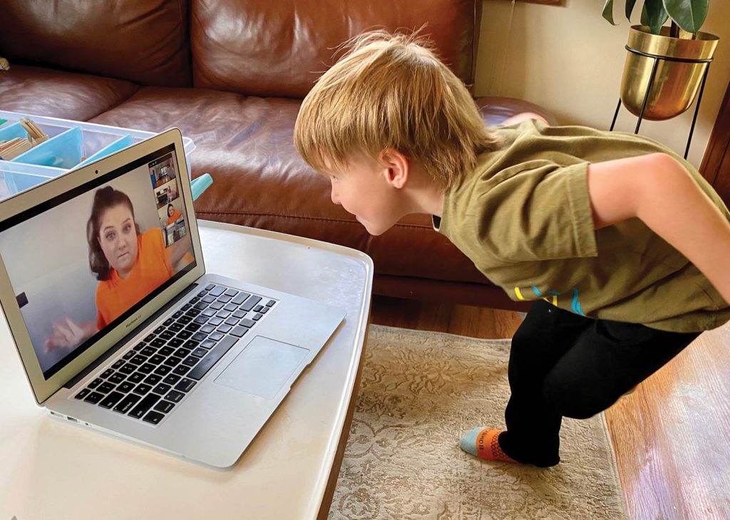 engaging with a woman on a video call. The room has a brown sofa and a patterned rug