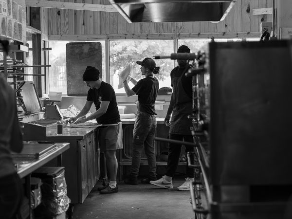 Inside the Shakespeare's pizza shop. 3 people are seen making pizzas in black and white.