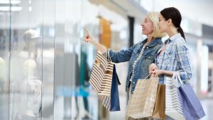 women with shopping bags pointing into a store window