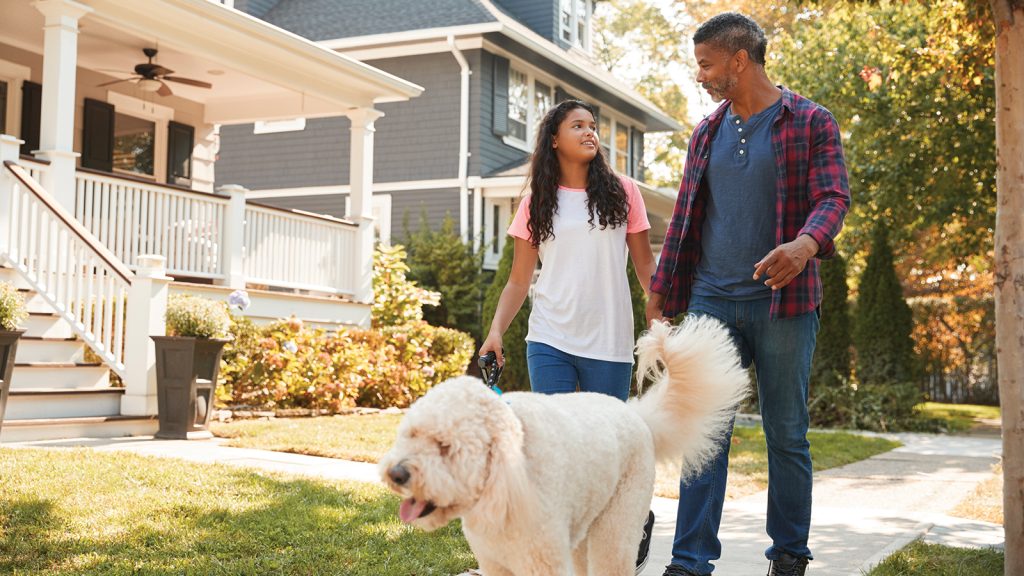Father And Daughter Walking Dog Along Suburban Street