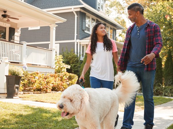 Father And Daughter Walking Dog Along Suburban Street