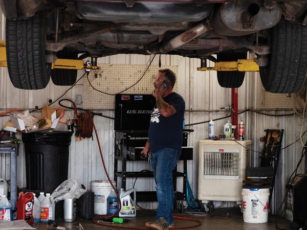 Tuning Spot owner on the phone in his garage with a car up on the lift
