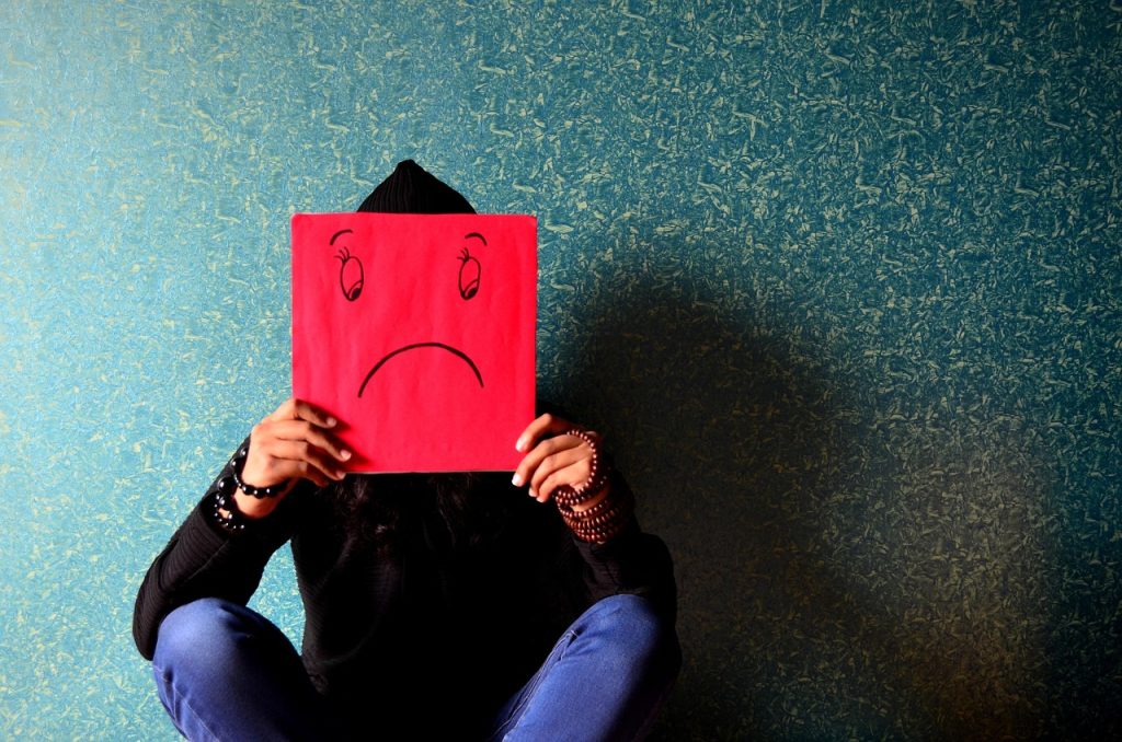 Illustration of someone seated in a shadow while holding a red sign marked with a frownie face.