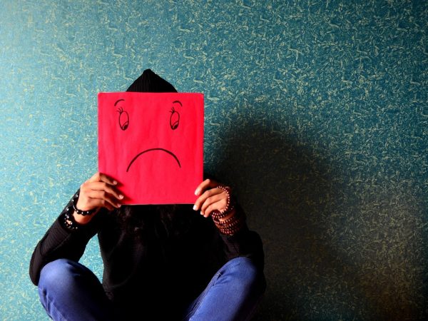 Illustration of someone seated in a shadow while holding a red sign marked with a frownie face.