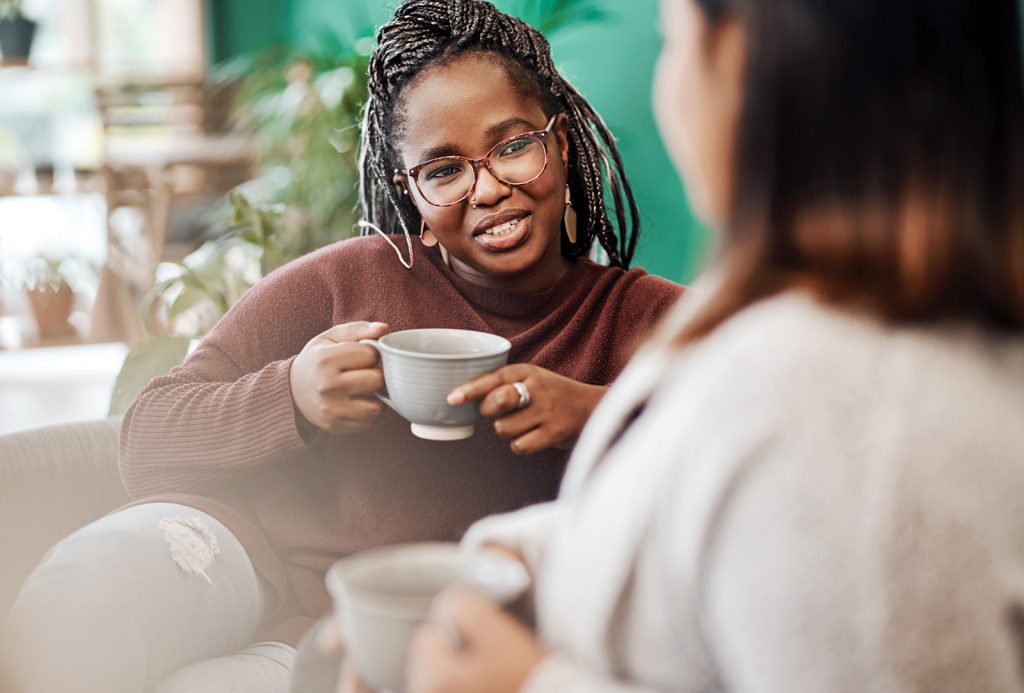Women, friends and relax with coffee on sofa for bonding with friendship, comfort and casual conversation. People, morning and warm beverage in afternoon with leisure, communication and happiness