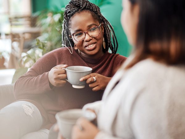Women, friends and relax with coffee on sofa for bonding with friendship, comfort and casual conversation. People, morning and warm beverage in afternoon with leisure, communication and happiness