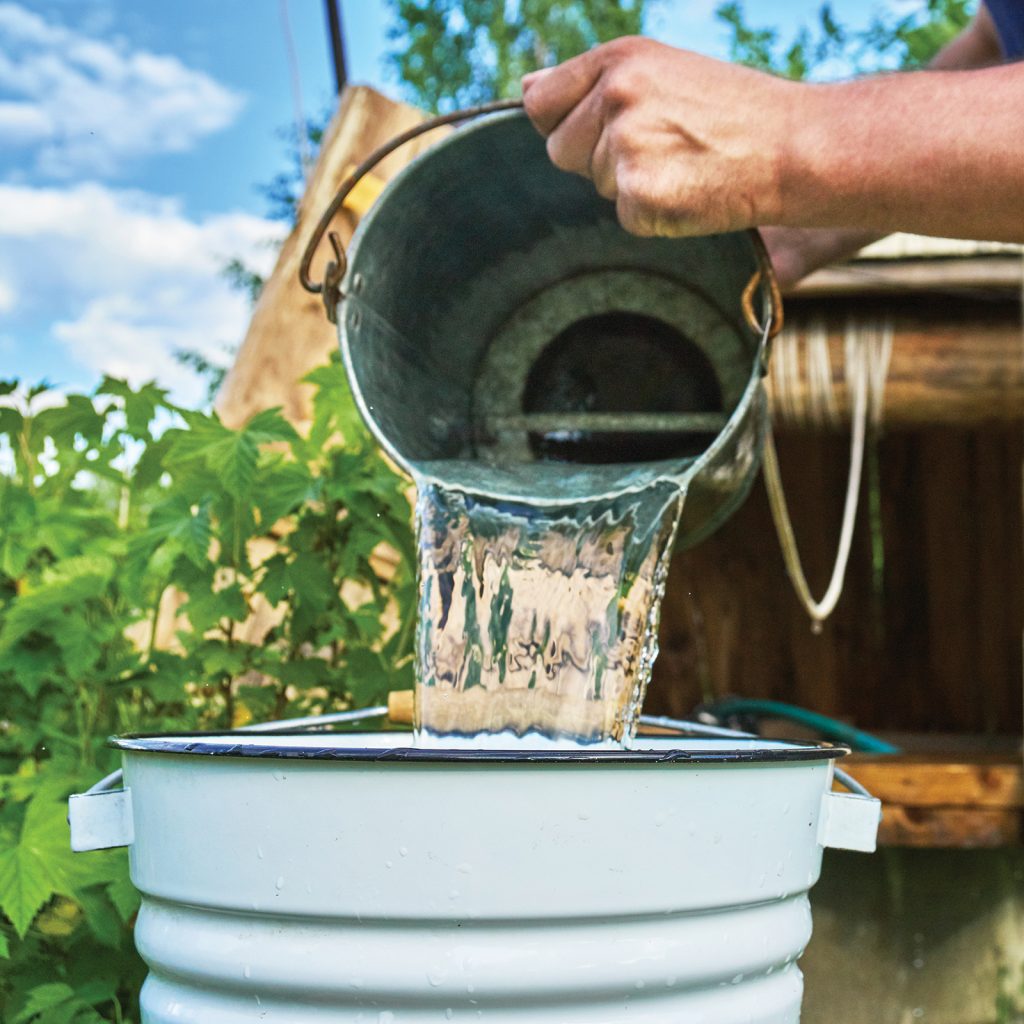 Man pouring water just taken up from a well into a enameled bucket